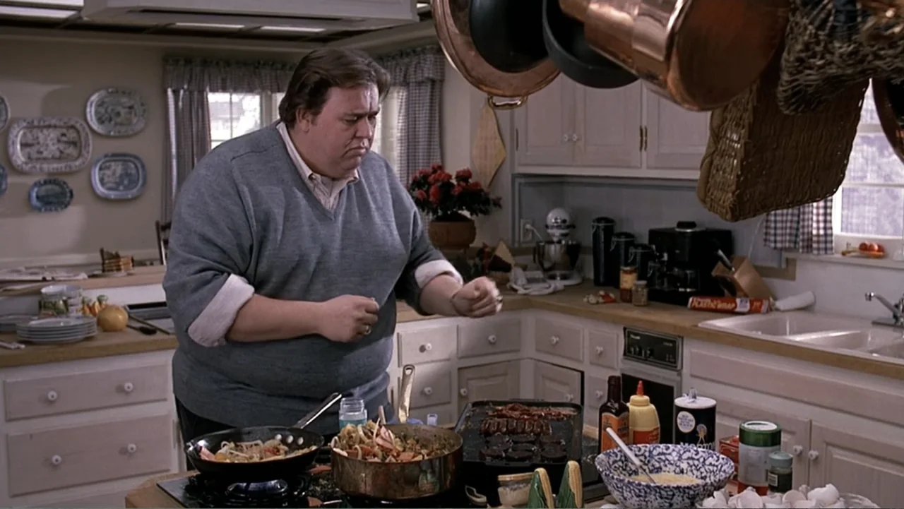 John Candy: I Like Me (2025) movie still: medium — A residential kitchen featuring light-colored cabinetry, copper cookware hanging overhead, and…