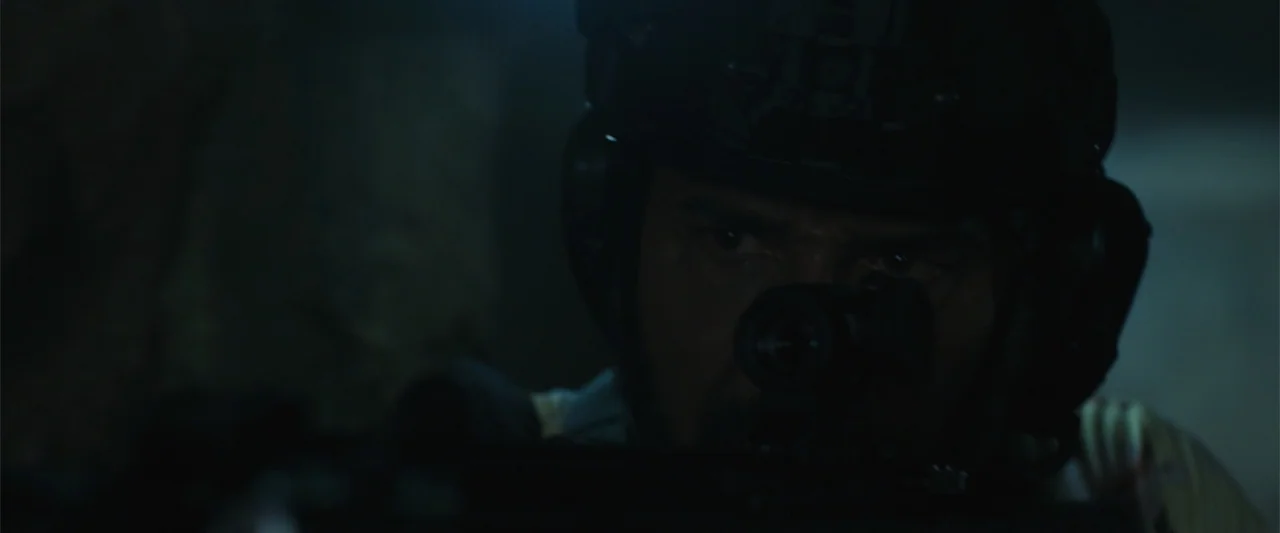 Trap House (2025) movie still: closeup — A dark, dimly lit environment obscures architectural details and surrounding space. A man wearing a…