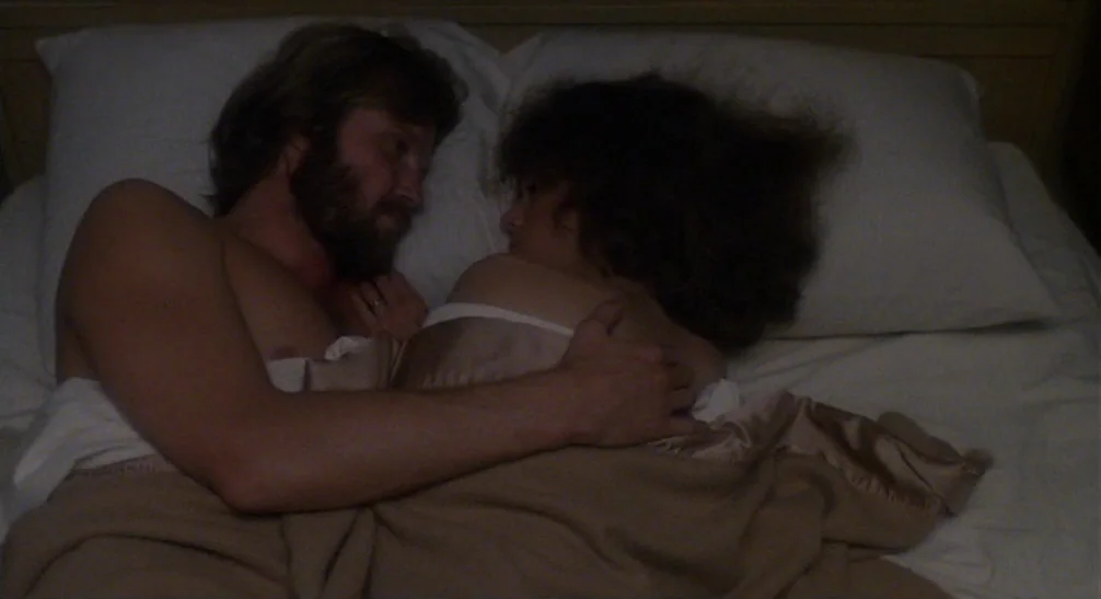 Coming Home (1978) movie still: medium — A man and a woman lie close together in a bed at night. They are covered by a beige blanket while facing…