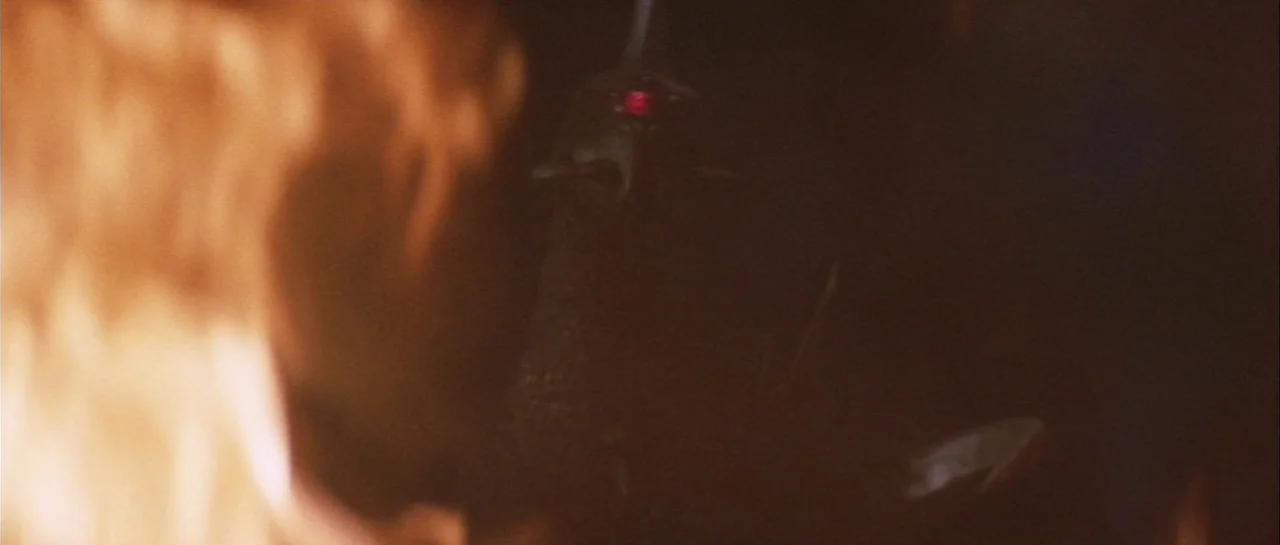 Godzilla Vs Gigan (1972) movie still: closeup — A dark, indistinct space is partially obscured by bright, blurred flames in the foreground. A small,…