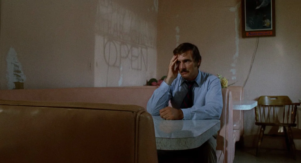 Duel (1971) movie still: medium — A sparsely decorated booth has pink vinyl seating and light beige walls. A man in a dress shirt sits alone with…