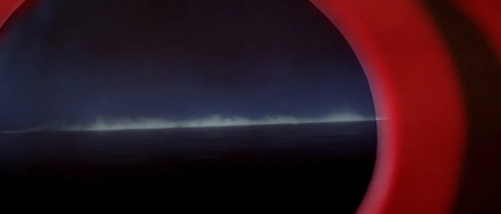 The Fog (1980) movie still: establishing — A view of the dark ocean horizon at night seen through an airplane window. The circular window edge is…