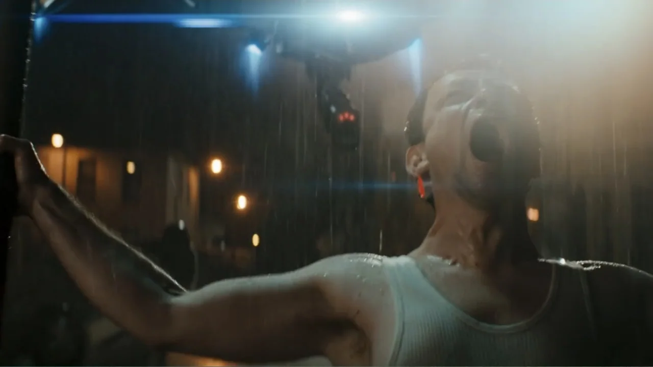 Robot Overlords (2015) movie still: medium — An urban street scene during a heavy rainstorm at night with blurred streetlights in background. A man…