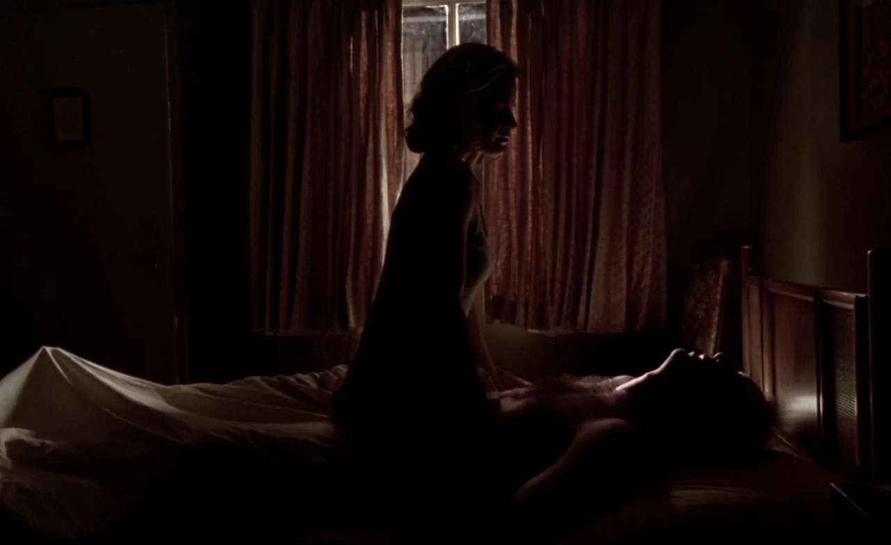 Leaving Las Vegas (1995) movie still: medium — A dimly lit room with draped curtains over a central window. A woman sits on top of a man resting in…