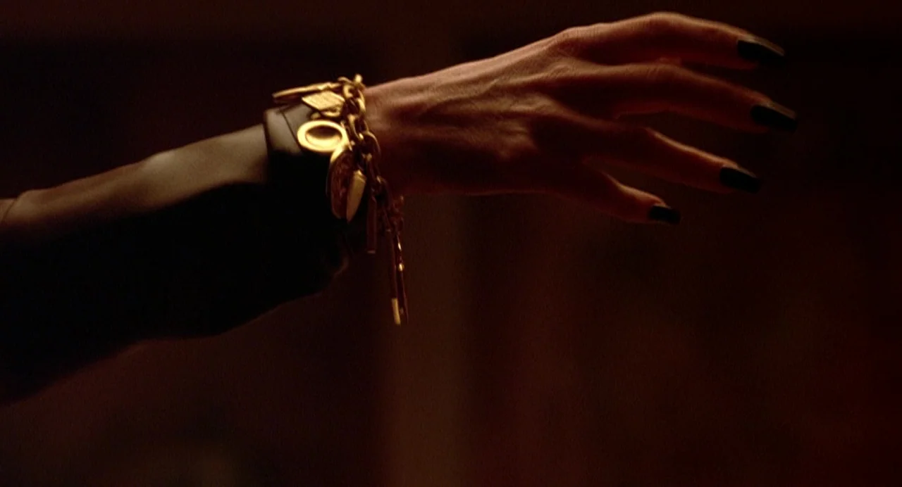 Office Killer (1997) movie still: closeup — A dark space provides a stark background for a human hand and wrist. A charm bracelet with gold…