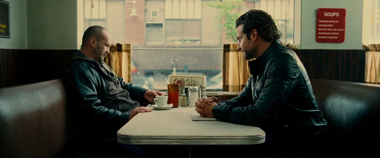 Limitless (2011) movie still: medium — A diner booth features brown vinyl seating and a formica table against a window. Two men in black leather…