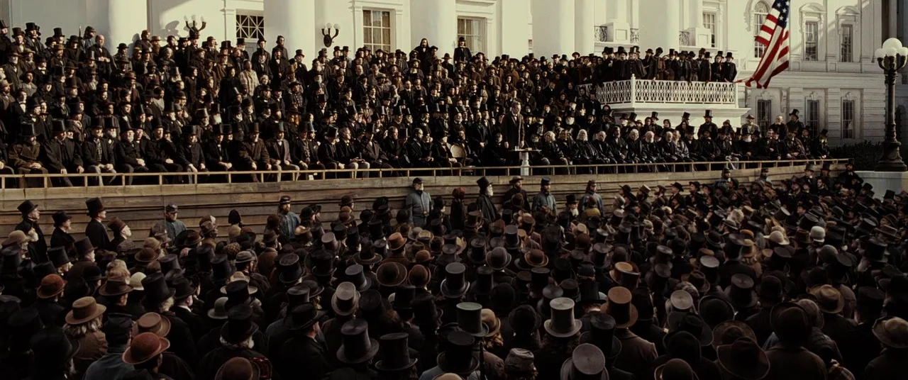 Lincoln (2012) movie still: wide — A vast crowd of men in nineteenth-century formal attire gathers before a white building. The individuals stand on…