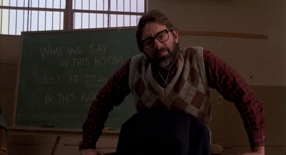 Raising Arizona (1987) movie still: medium — A man stands in front of a green chalkboard in a room. The chalkboard displays handwritten text about…