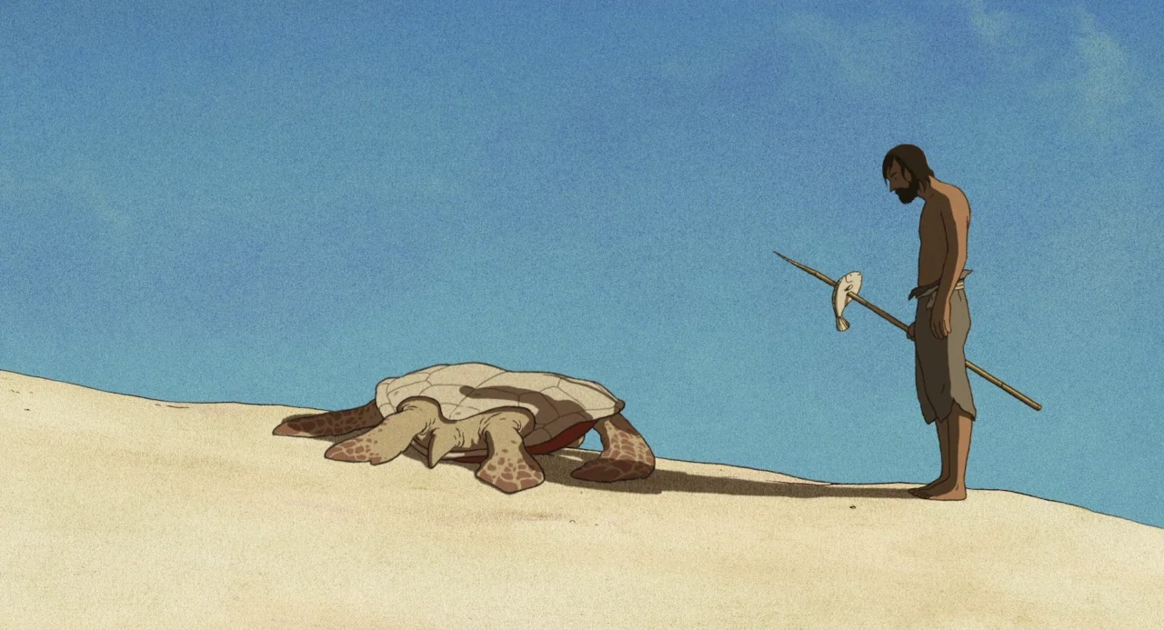The Red Turtle (2016) movie still: wide — A man stands on a wide sandy beach under a clear blue sky. He watches a large turtle resting on the ground…