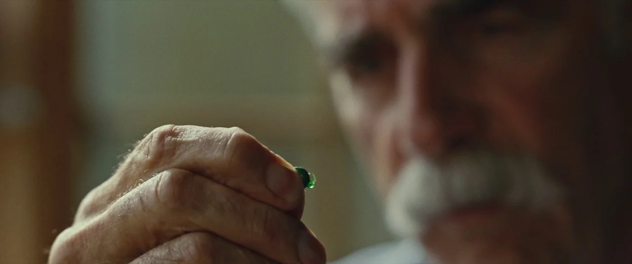The Man Who Killed Hitler and Then the Bigfoot (2018) movie still: closeup — A man holds a small green pill between his thumb and forefinger. The…