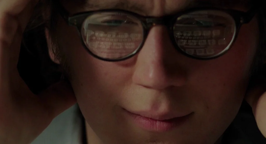 Ruby Sparks (2012) movie still: closeup — A dark, cramped interior space frames a person working at a desk. The subject stares ahead while an…