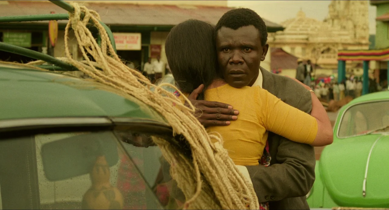 Mississippi Masala (1991) movie still: medium — A bustling city street features vintage green cars and buildings in the background. A man embraces a…
