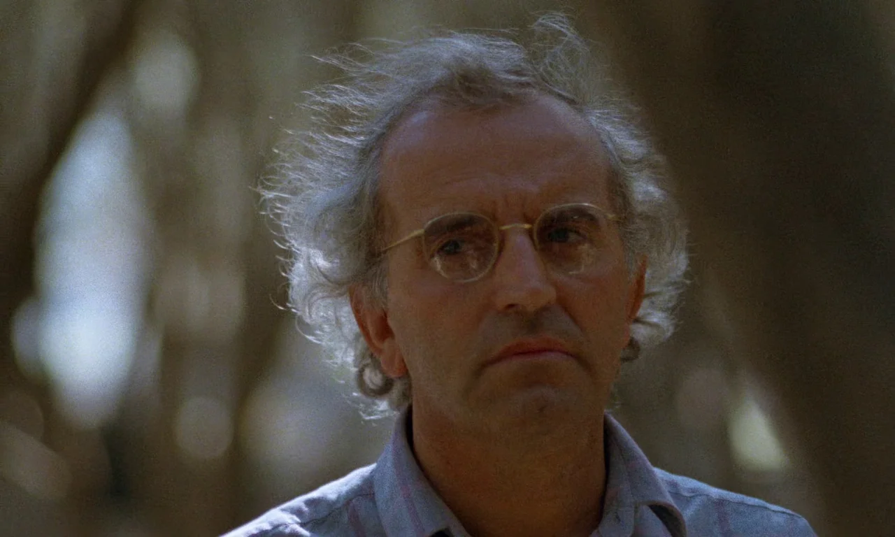 Life, and Nothing More (1992) movie still: closeup — A man stands outdoors with blurred tree trunks visible in the background. He looks slightly…