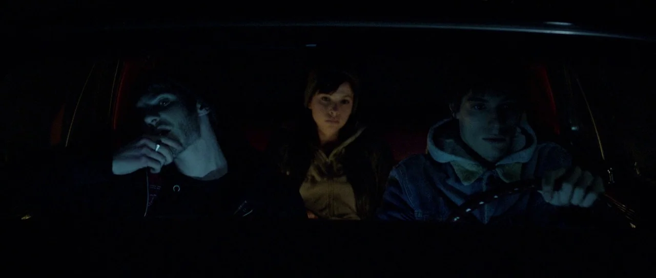 Livid (2011) movie still: medium — Three young adults sit in the front and middle seats of a dark car. The interior is illuminated by low-intensity…
