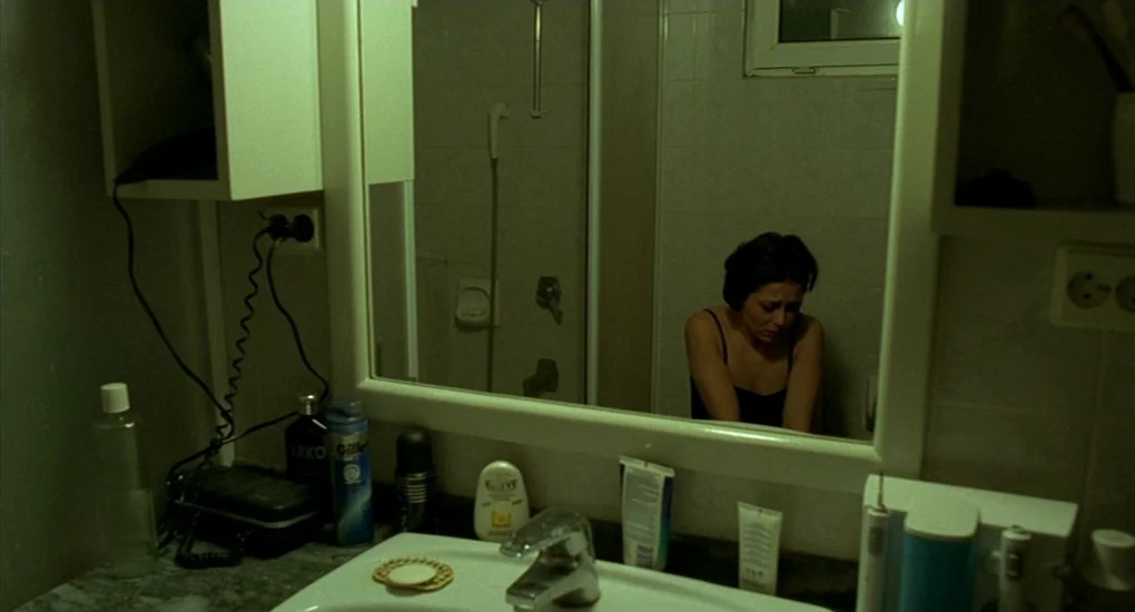 Uzak (2002) movie still: A woman sits in a cramped bathroom, her image captured in the vanity mirror as she reflects on her personal turmoil. The…