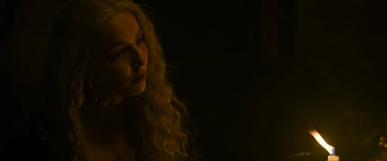 The Last Duel (2021) movie still: closeup — A dimly lit stone chamber is shrouded in heavy darkness. A woman with long blonde hair sits illuminated…