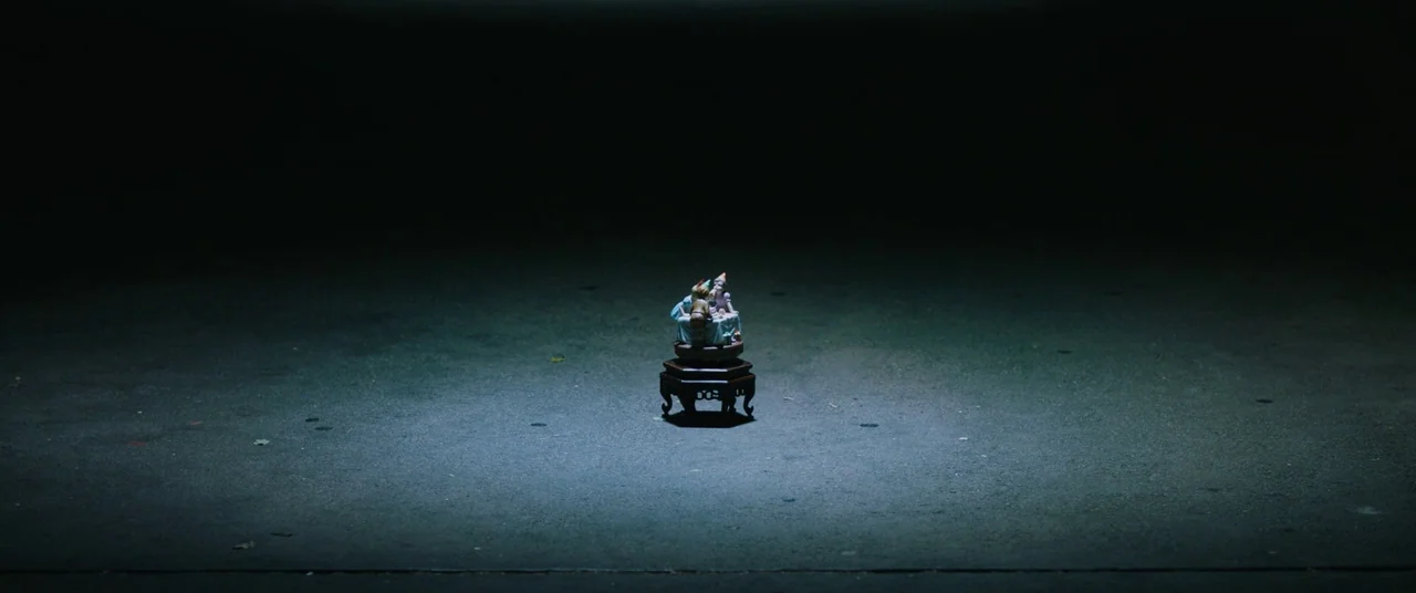 Happy Death Day (2017) movie still: wide — A small decorative figurine stands on a wooden pedestal placed on dark asphalt ground. A tight pool of…