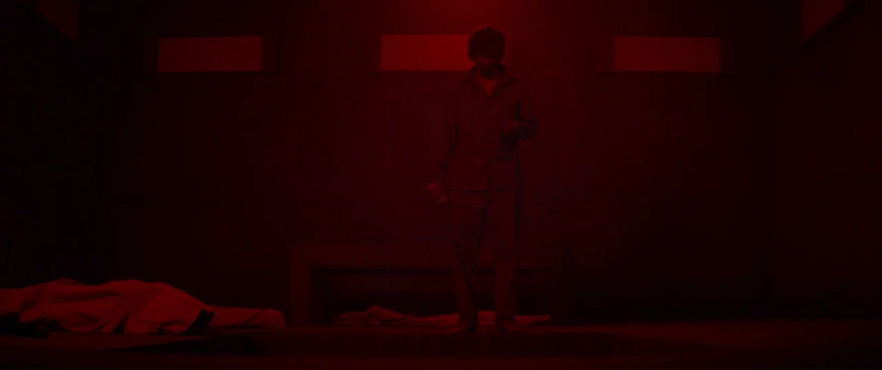 The Platform (2019) movie still: fullbody — A dimly lit room features a central subject standing before a recessed floor opening. A white sheet lies…