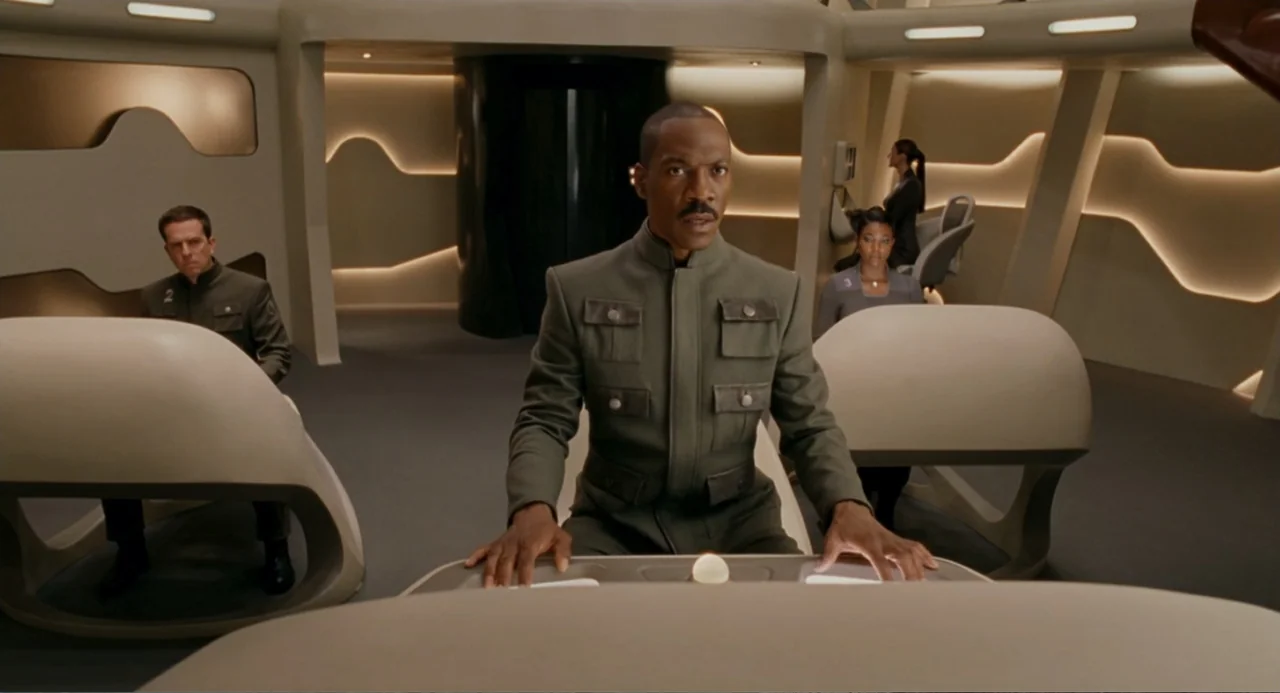 Meet Dave (2008) movie still: medium — A modern, minimalist bridge of a spaceship features curved white walls and modular seating. A man sits at a…