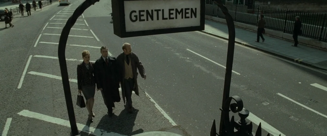 Harry Potter & The Deathly Hallows Part 1 (2010) movie still: wide — A London city street features a black metal archway holding a GENTLEMEN sign.…