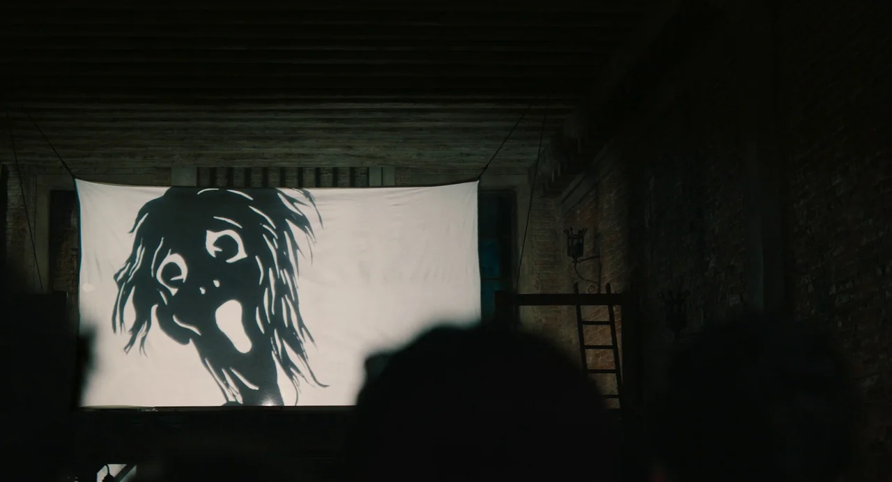 A Haunting In Venice (2023) movie still: wide — A dark, unfinished attic space features brick walls and exposed ceiling beams. A large white sheet…