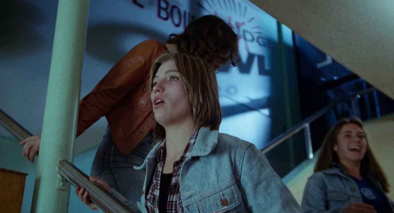 Out of the Blue (1980) movie still: medium — Three young women ascend a staircase within a building with a large neon sign. They are looking toward…