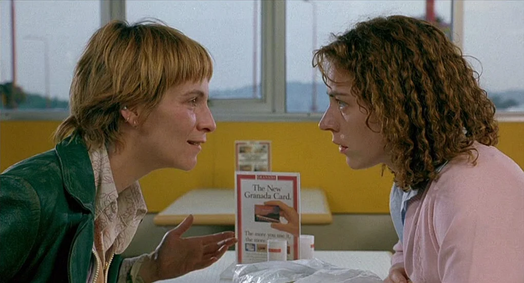 Butterfly Kiss (1995) movie still: medium — Two women sit opposite each other in a brightly lit diner booth. They are facing each other while…