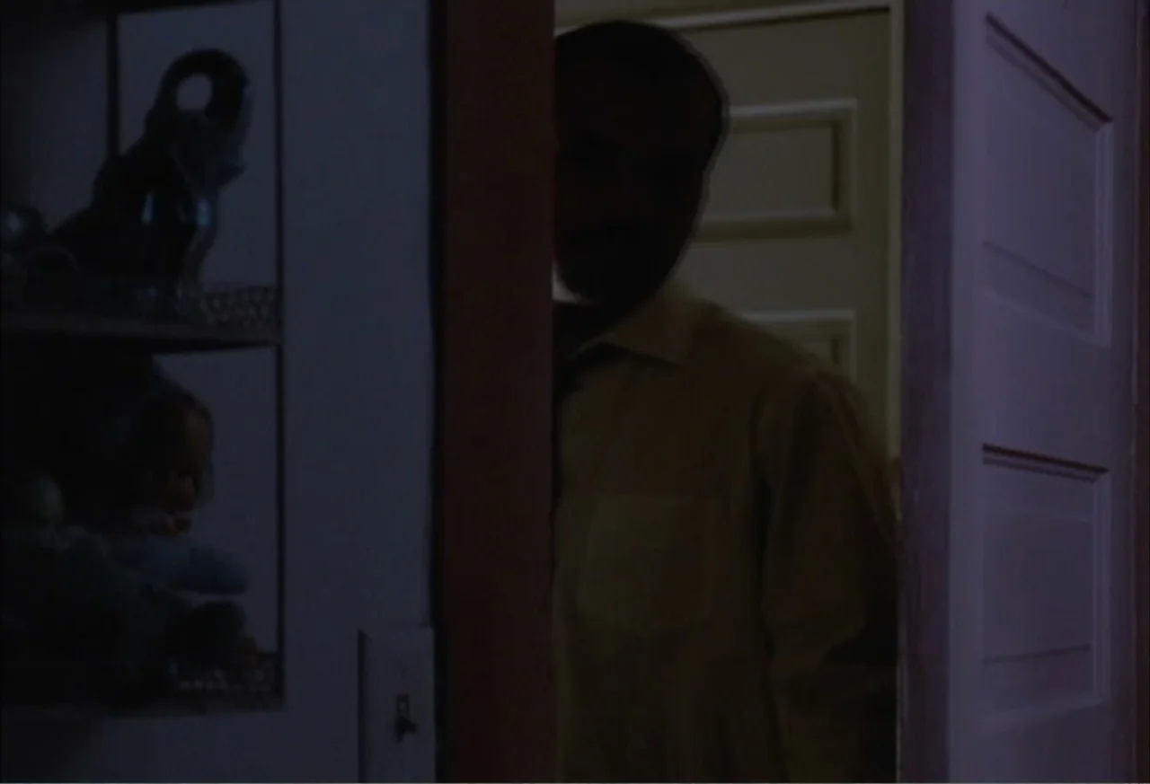 Boycott (2001) movie still: medium — A dimly lit room interior features a person standing in a dark doorway. The subject is mostly silhouetted…