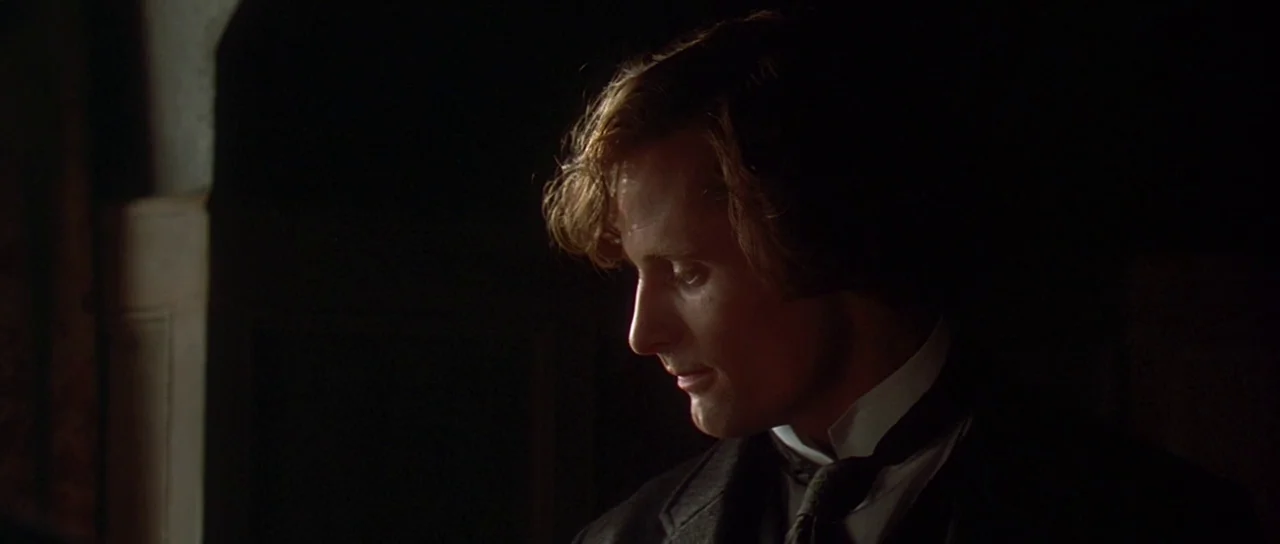 The Portait of a Lady (1996) movie still: closeup — A dark indoor space with minimal visible background details and deep shadows. A man in formal…
