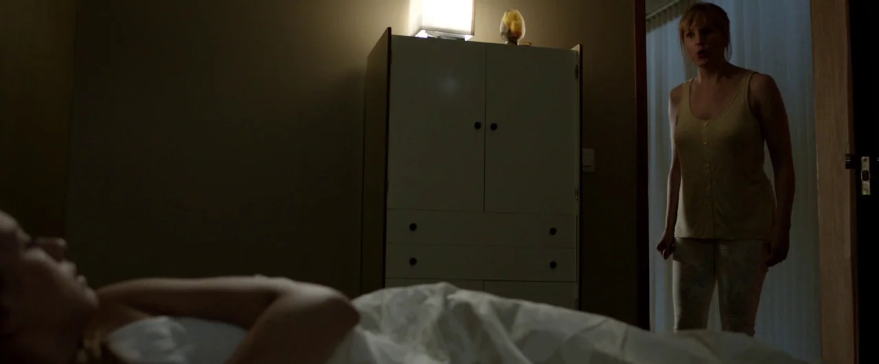 Borgman (2013) movie still: medium — A dimly lit room with a white cabinet and a bed with white sheets. A woman stands in the doorway while another…