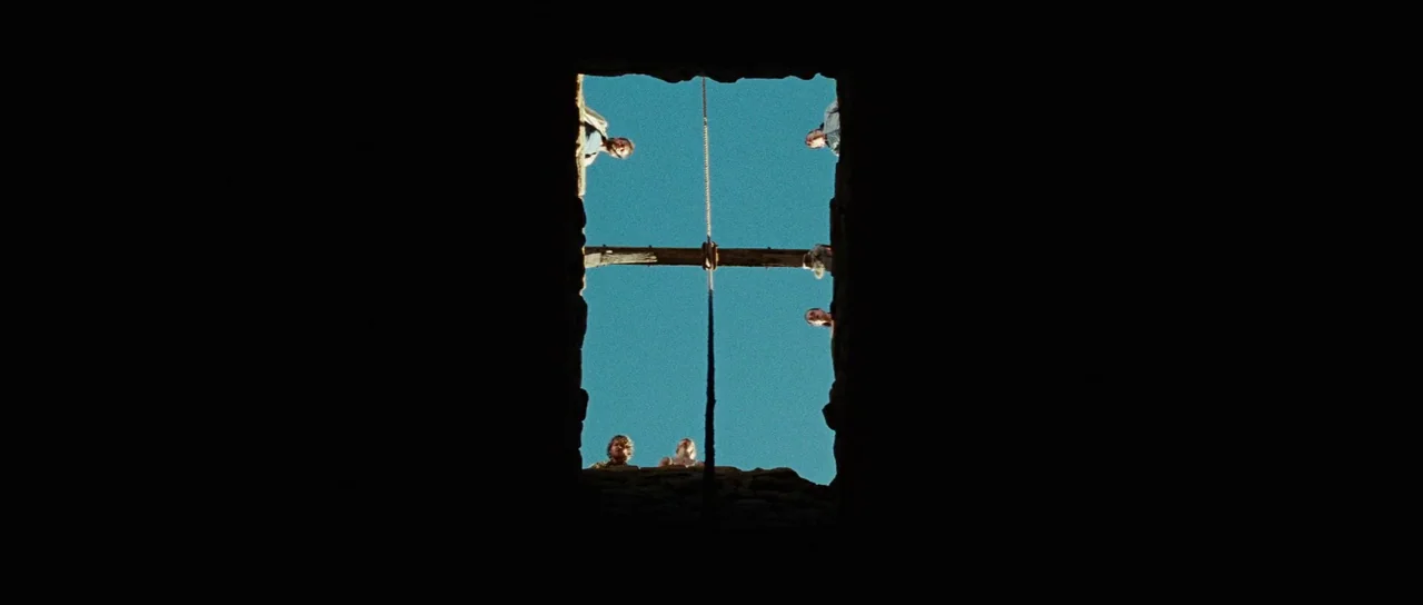 The Ruins (2008) movie still: wide — A deep vertical stone shaft viewed from below looking up at the bright sky. Several people stand at the top…
