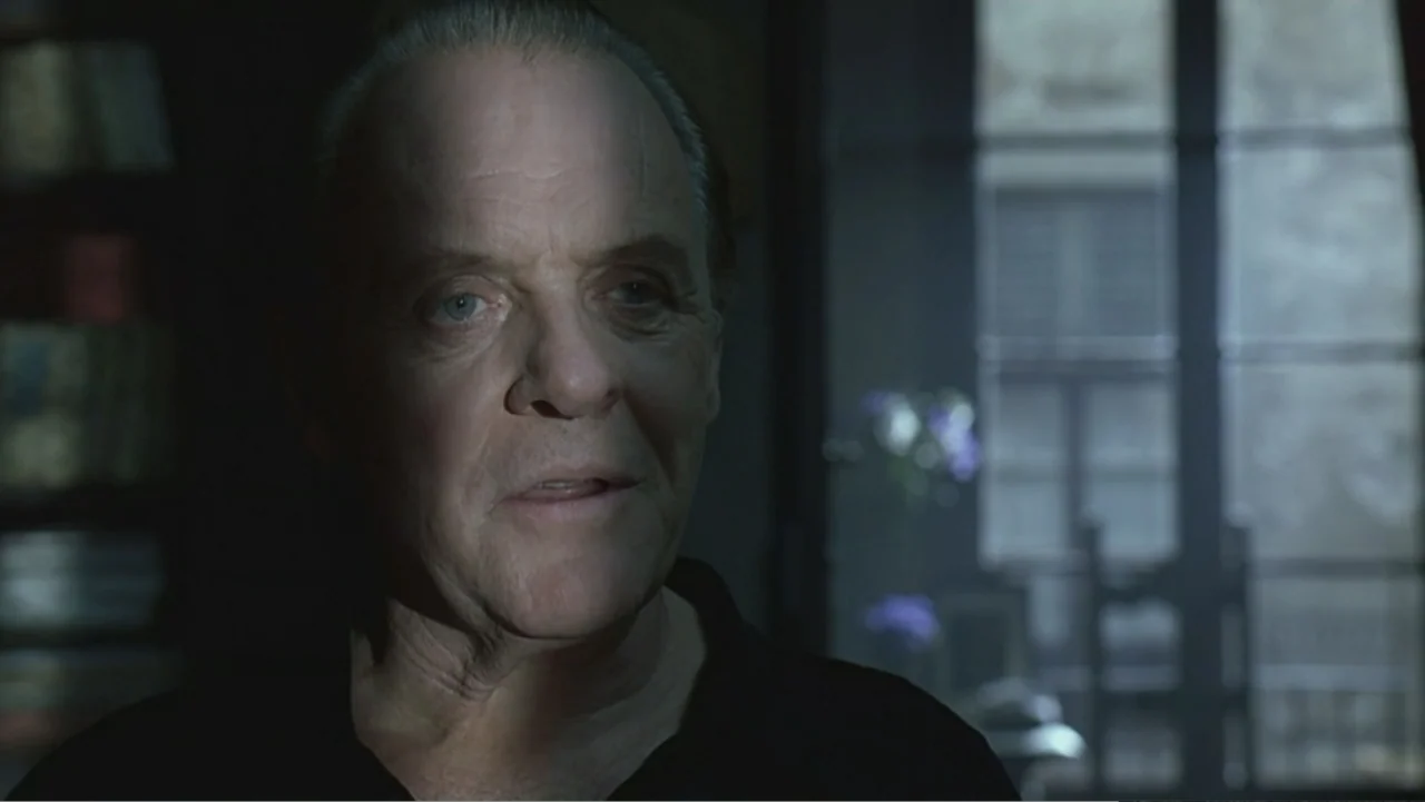 Hannibal (2001) movie still: closeup — A dimly lit indoor study features a large window with blue curtains. An elderly man stands in the foreground…