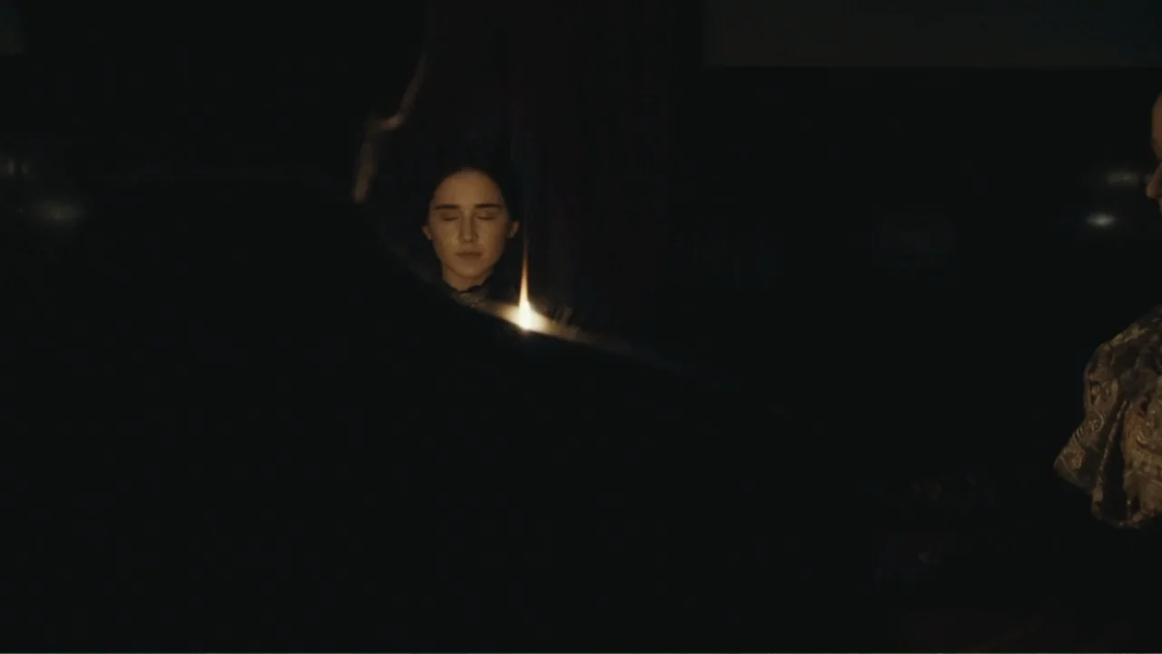 Demon in the White House (2021) movie still: medium — A dark, dimly lit indoor setting features a flickering candle on a table. A woman with closed…
