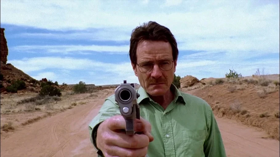 Breaking Bad (2008) movie still: medium — A dry dirt road stretches through a barren, arid landscape under an open sky. A middle-aged man stands in…