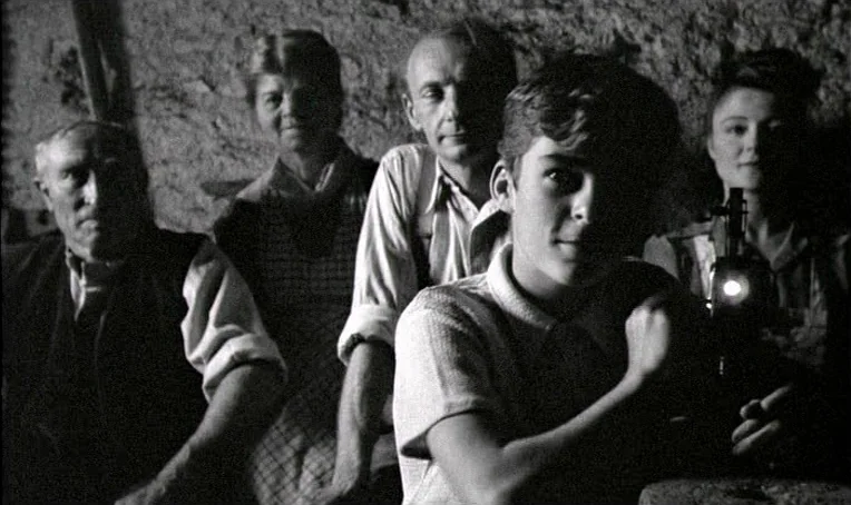 Jacquot de Nantes (1991) movie still: medium — A group of four people in a dark cellar with stone walls and textured surfaces. They sit together as…
