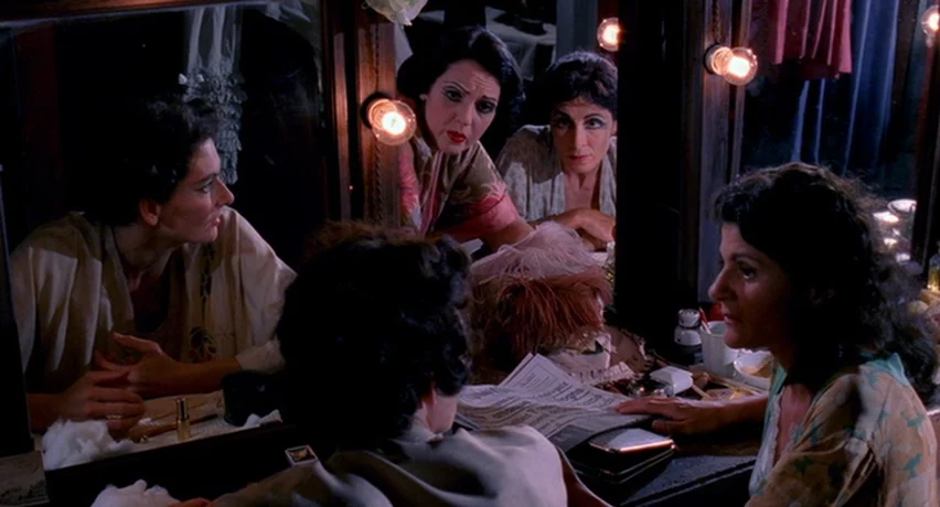 The Man Who Cried (2000) movie still: medium — A dimly lit dressing room contains multiple mirrors and vanity lights attached to the wall. Four…