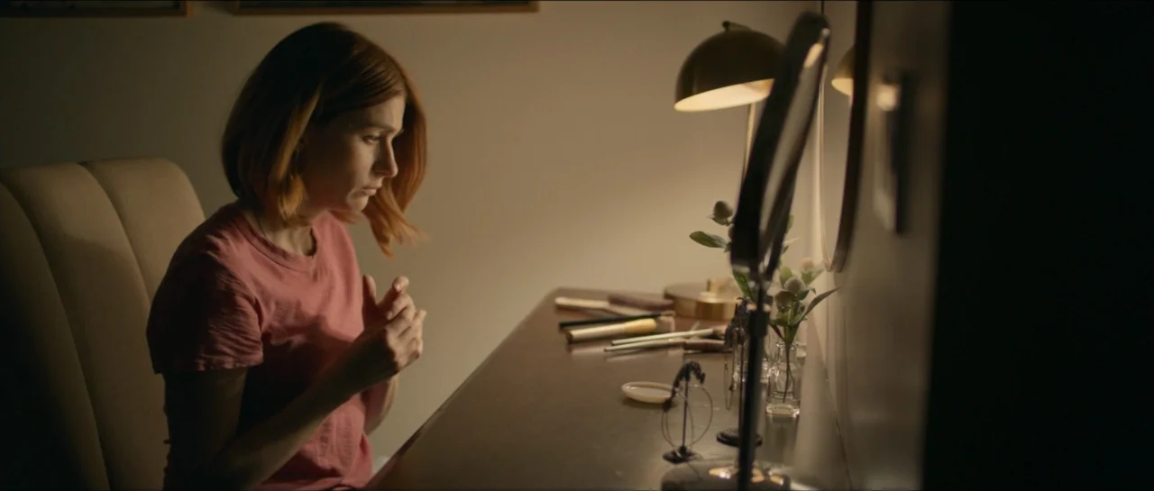 We Broke Up (2021) movie still: medium — A dimly lit room contains a wooden vanity table with small trinkets and makeup. A woman sits on a chair…