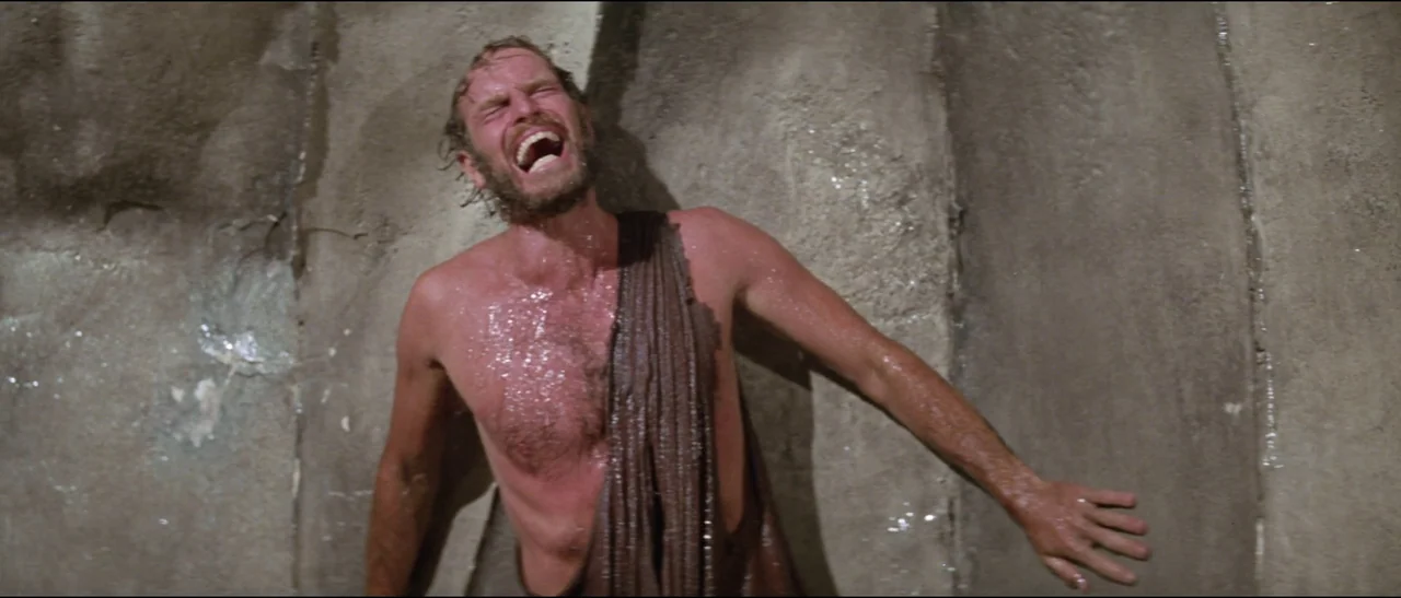Planet of the Apes (1968) (1968) movie still: medium — A man stands before a rough-textured stone wall in an outdoor setting. He leans against the…