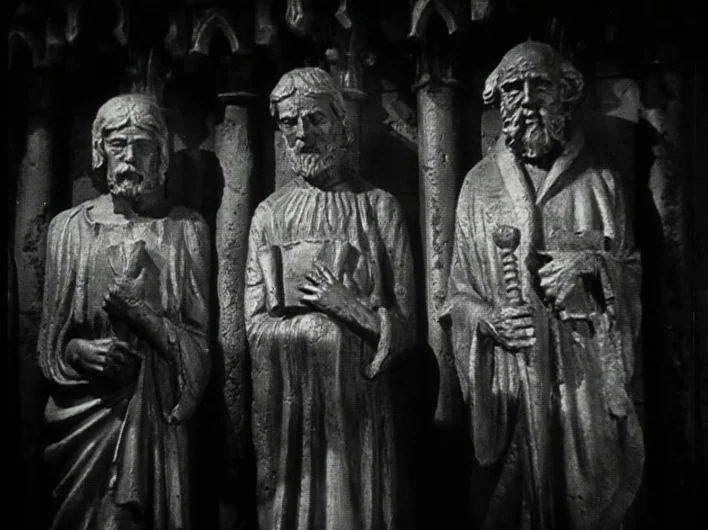 The Man Who Laughs (1928) movie still: fullbody — Three weathered stone statues stand side by side against a complex gothic stone wall. The figures…