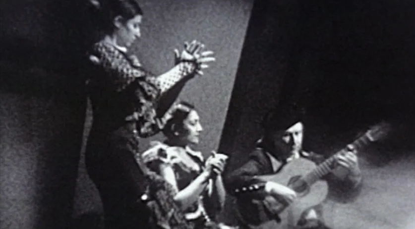 The Saddest Music in the World (2003) movie still: medium — A dimly lit room with a textured wall behind the performers. Three musicians and dancers…