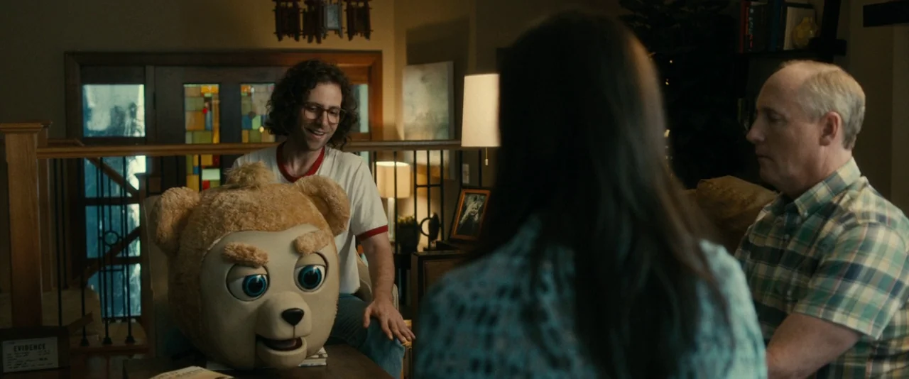 Brigsby Bear (2017) movie still: medium — An interior space features a man gesturing toward a large bear prop on a table. An older man and a woman…
