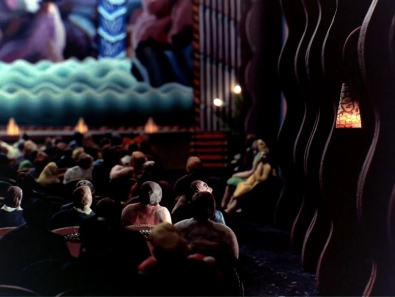 Asparagus (2007) movie still: medium — A dimly lit indoor auditorium features rows of seated people facing a large projection screen. The audience…