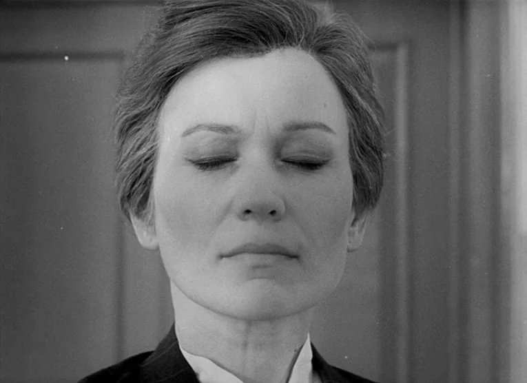 Wings (1966) movie still: closeup — A close-up shot of a woman with short dark hair in a simple interior. She stands perfectly still with her eyes…
