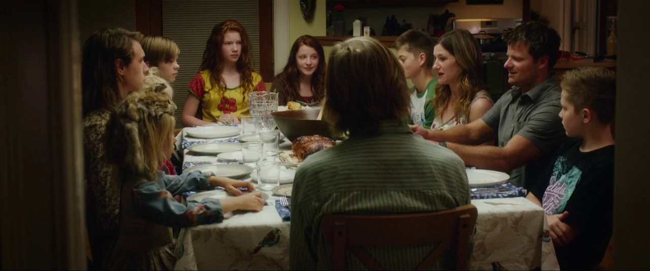 Captain Fantastic (2016) movie still: wide — A family sits around a rectangular dining table for an evening meal at home. The table is set with…