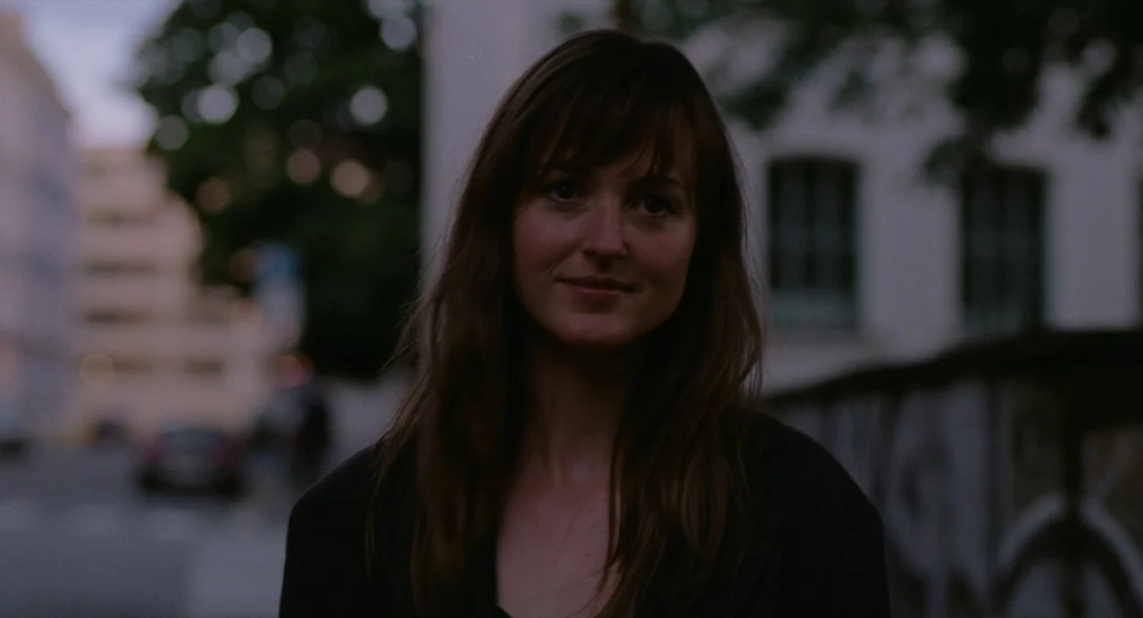 The Worst Person in the World (2021) movie still: medium — A city street at blue hour with blurred background buildings and trees. A woman stands in…