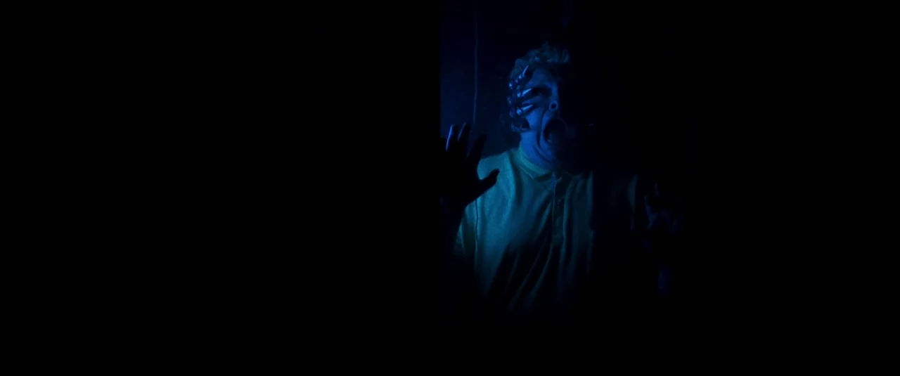 Mandy (2018) movie still: medium — A person is framed within a narrow vertical light opening in total darkness. The subject stands behind a…