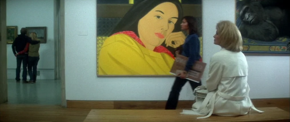 Dressed to Kill (1980) movie still: medium — A spacious art gallery with white walls and polished wooden floors. A woman sits on a bench while…