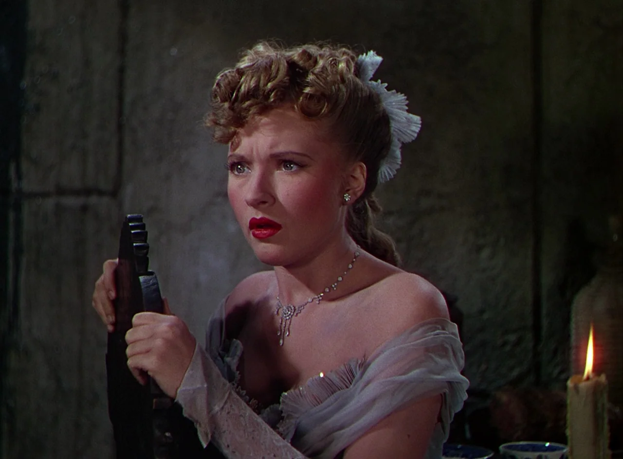 Phantom of the Opera (1943) movie still: medium — A dark stone-walled room provides the background for a woman in an evening dress. The woman holds…