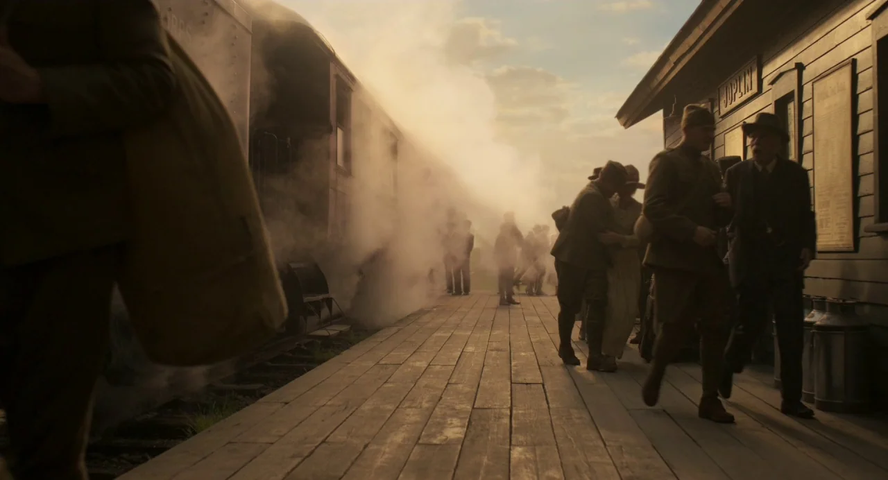 Dumbo (2019) movie still: wide — A wooden train station platform marked Joplin is filled with steam from a locomotive. People in 1940s period…