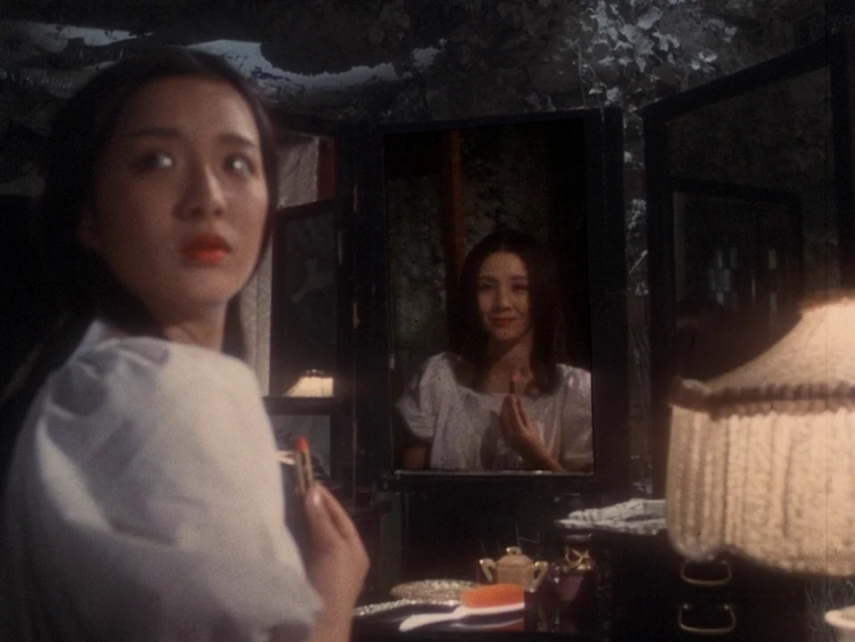 House (Hausu) (1977) movie still: medium — A woman sits before a tripartite mirror in a dimly lit room with vintage furniture. She holds a small…
